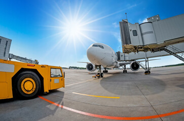 Parking at the airport, airplane at the teletrap. Aerodrome tractor is ready for towing and departure of the aircraft. Against the background of a blue sky and bright sun, nice weather.