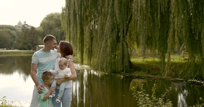 Young family with two children outdoors by the river in summer playing
