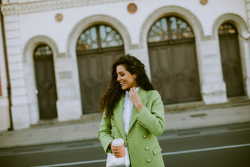 Young woman using smartphone on the street and holding takeaway coffee