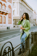 Young woman using smartphone on the street and holding takeaway coffee