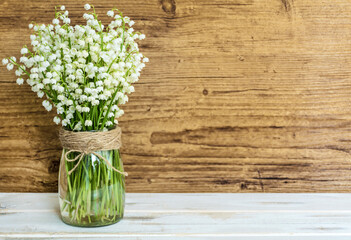 Lily of the Valley Bouquet in Glass Vase on Wooden  Background with Copy Space .Spring Flowers Background