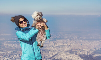 Happy  Young Woman Hugging her Havanese Muddy Dog Outdoor  in the Winter Mountain with City View