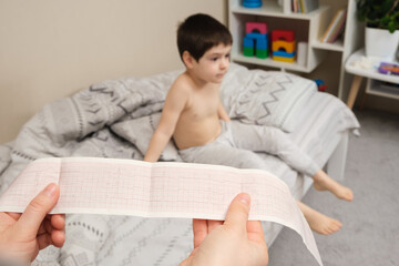 ECG film in the hands of a pediatrician cardiologist against the background of a boy of 4 years....