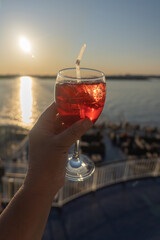 A glass with red wine in hand against the background of the deck of the ship and the sunset on the sea. Sunny, summer evening. Sea cruise. There is space for text. Peace, love concept