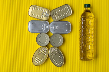 Tin cans next to a bottle of sunflower oil, on a yellow background.