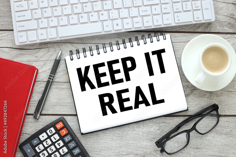 Poster keep it real text on notebook near computer keyboard