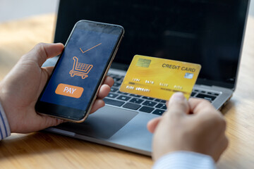A person is holding a credit card to pay online, credit card payments can be used on both laptop computers and mobile phones. Concept of payment for goods and services via credit card.