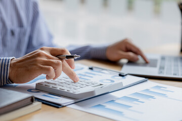 Businessman using a calculator to calculate numbers on a company's financial documents, he is analyzing historical financial data to plan how to grow the company. Financial concept.