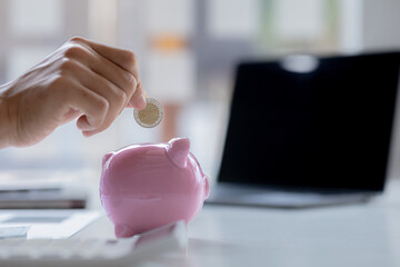 Obraz na płótnie Canvas A businessman is putting coins into a pink pig piggy bank, he is saving for investments, money growth, stock investments. The idea of investing money to make it worthwhile to grow and be sustainable.