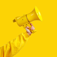 a woman's hand in yellow clothing holds a yellow megaphone on a yellow background. alarm