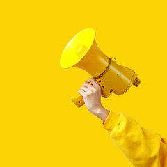 a woman's hand in yellow clothing holds a yellow megaphone on a yellow background. alarm