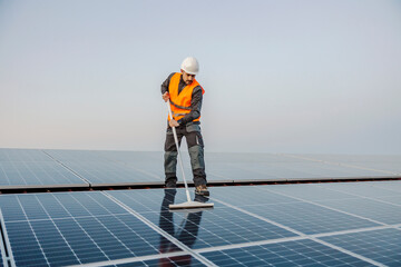 A worker standing on the roof and cleaning solar panels from dirt.