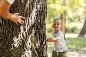 A happy little boy playing hide and seek with his father in the forest.