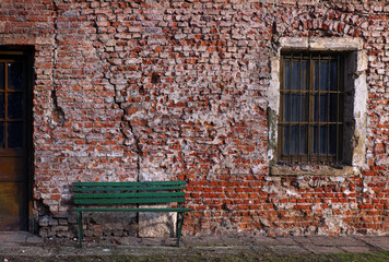 Fototapeta na wymiar An old green bench on the background of a ruined red brick wall ... 