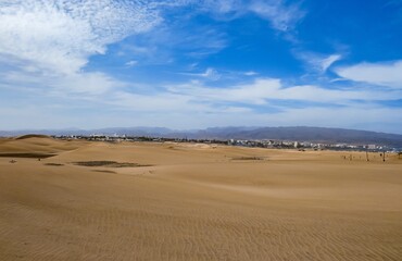 Fototapeta na wymiar Hoteles y Resorts en la distancia detrás de las dunas costeras de la playa de Maspalomas, isla de Gran Canaria, España. Paisaje desértico y costero diseñado por el efecto del viento sobre la arena.