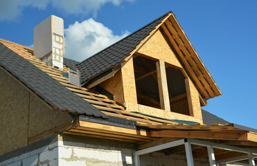 Roofing construction on the stage of metal tiles installation on a gable roof with a dormer using flashing, and unfinished brick chimney. Roofing Construction. Attic insulation.