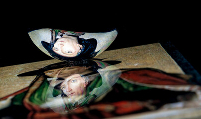 A classic renaissance portrait reflect from a tablet surface into a spoon with a black background