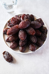 Medjoul dates in a white plate and glass of water on a gray background.