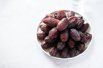 Medjoul dates in a white plate and glass of water on a gray background. Overhead view.