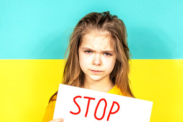 The face of a crying girl close-up. The girl holds a STOP poster in her hands against the background of the Ukrainian flag. Stop the war in Ukraine. The concept of peace in Ukraine. Children against