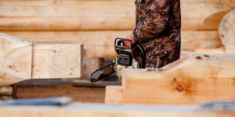 Industrial work carpenter sawing with chainsaw log, construction frame building site of house made...