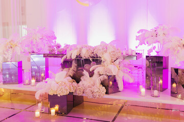 The elegant and colorful area of the Newlyweds table is decorated with flowers and illuminated with violet light. Beautiful decoration of the wedding table.