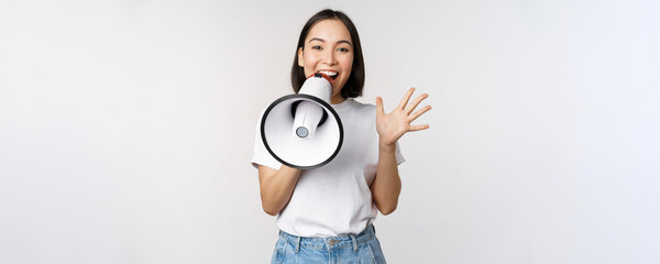 Happy asian woman shouting at megaphone, making announcement, advertising something, standing over...