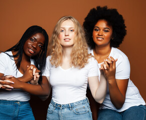 young pretty african and caucasian women posing cheerful together on brown background, lifestyle diverse nationality people concept