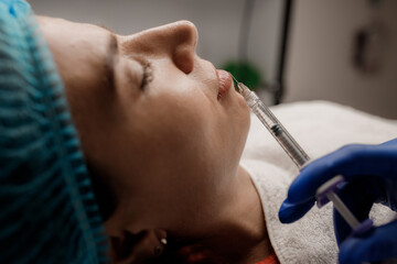 A cosmetologist injects a syringe into a patient
