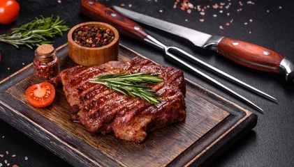 Gordijnen Grilled ribeye beef steak, herbs and spices on a dark table © chernikovatv
