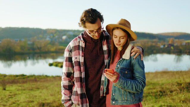 Young couple man and woman use phone in the forest near lake feel happy smiling. Social networking outdoors. Portrait. Close up. Slow motion