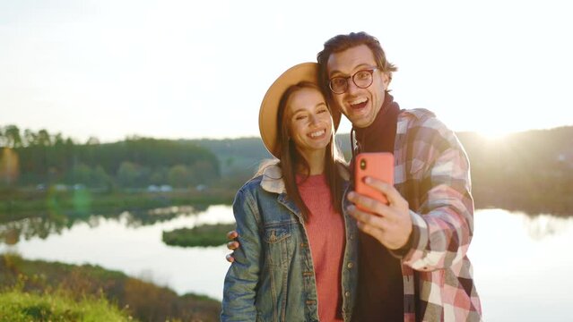 Happy young smiling couple use phone and take selfie in the forest near lake. Nature mobile relationship. Outdoors. Romantic. Close up. Slow motion