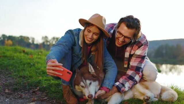 Shot of happy couple with a dog taking selfie photo on phone in autumn forest near lake. Landscape vacation relationship pets. Outdoors nature. Slow motion