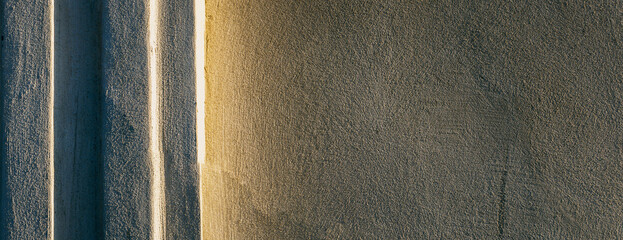 Naturalne tło podświetlonej promieniami zachodzącego słońca ściany muru. Tekstura  pęknięć z strukturą tynku.  Panorama, tło, tapeta.
