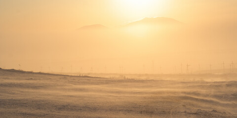 Winter arctic landscape. View of the snow-covered tundra and mountains in frosty fog. Golden sunlight at sunset. Cold snowy and windy weather. Blowing snow. Polar climate. Chukotka, Siberia, Russia.