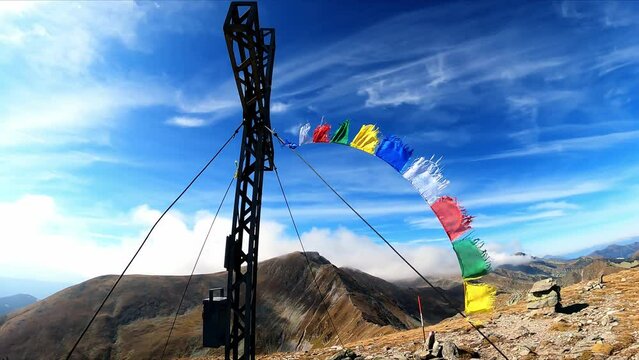 The summit cross of mount Seckauer Zinken in the Seckau Tauern in Styria, Austria. Nepalese or Tibetan prayer flags are attached to the cross and strong wind is blowing. Freedom in the Austrian Alps
