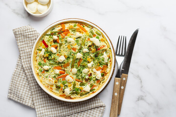 Egg frittata omelet with seasonal vegetables and cheese in plate on white marble background. Top view healthy diet food concept