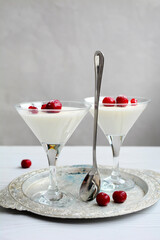 vertical composition. Glasses with delicious panna cotta garnished with cherries on a tray on a light background