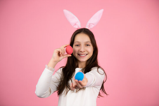 Happy brunette girl wearing rabbit ears on head holding in her hands two painted eggs in red and blue color, Easter concept.