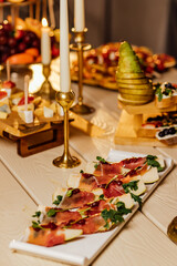 Prosciutto with pear and basil on a black stone plate. Jamon. Italian antipasto. Top view.