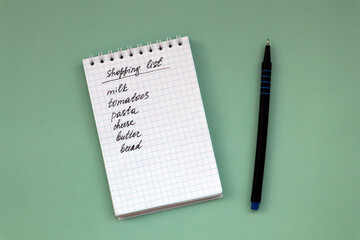 Notebook with shopping list on green background and pen with copy space.