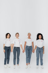 Obraz premium Multiethnic women with ribbons of breast cancer awareness holding hands on grey background.