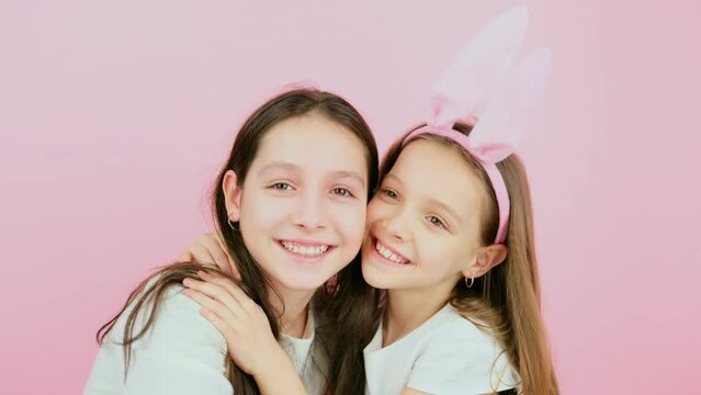 Two caucasian sisters are having joy together on Easter holiday, embracing each other and kissing on cheek.