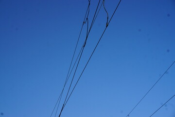 Elektrische Leitungskabel über Bahnschienen vor blauem Himmel am Abend im Winter