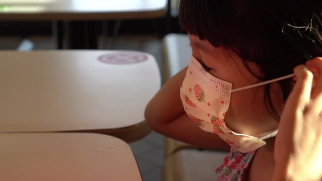 Little girl wear back the dace mask after finish eat the food at restaurant