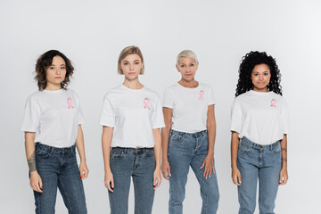Obraz premium Interracial women with ribbons of breast cancer awareness looking at camera isolated on grey.