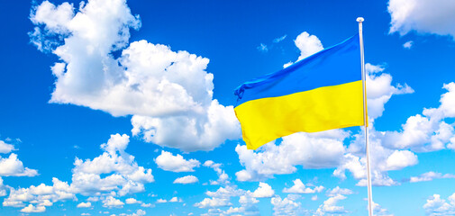 Waving Ukraine flag against blue sky with clouds. Peace for Ukraine concept.