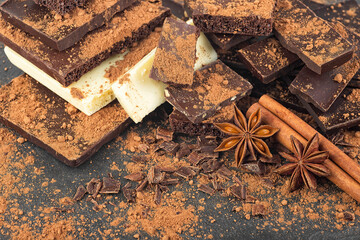 Broken chocolate pieces, cocoa powder, cinnamon sticks and anise stars on a black background