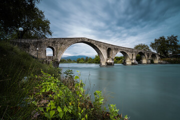 Fototapeta na wymiar Stone arch bridge over river in Arta city, Greece.