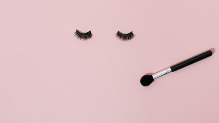 False eyelashes and makeup brush on pastel pink background with copy space. Minimal beauty, get ready concept. Makeup accessories, cosmetics products. Top view, flat lay, fake eyelashes, web banner.